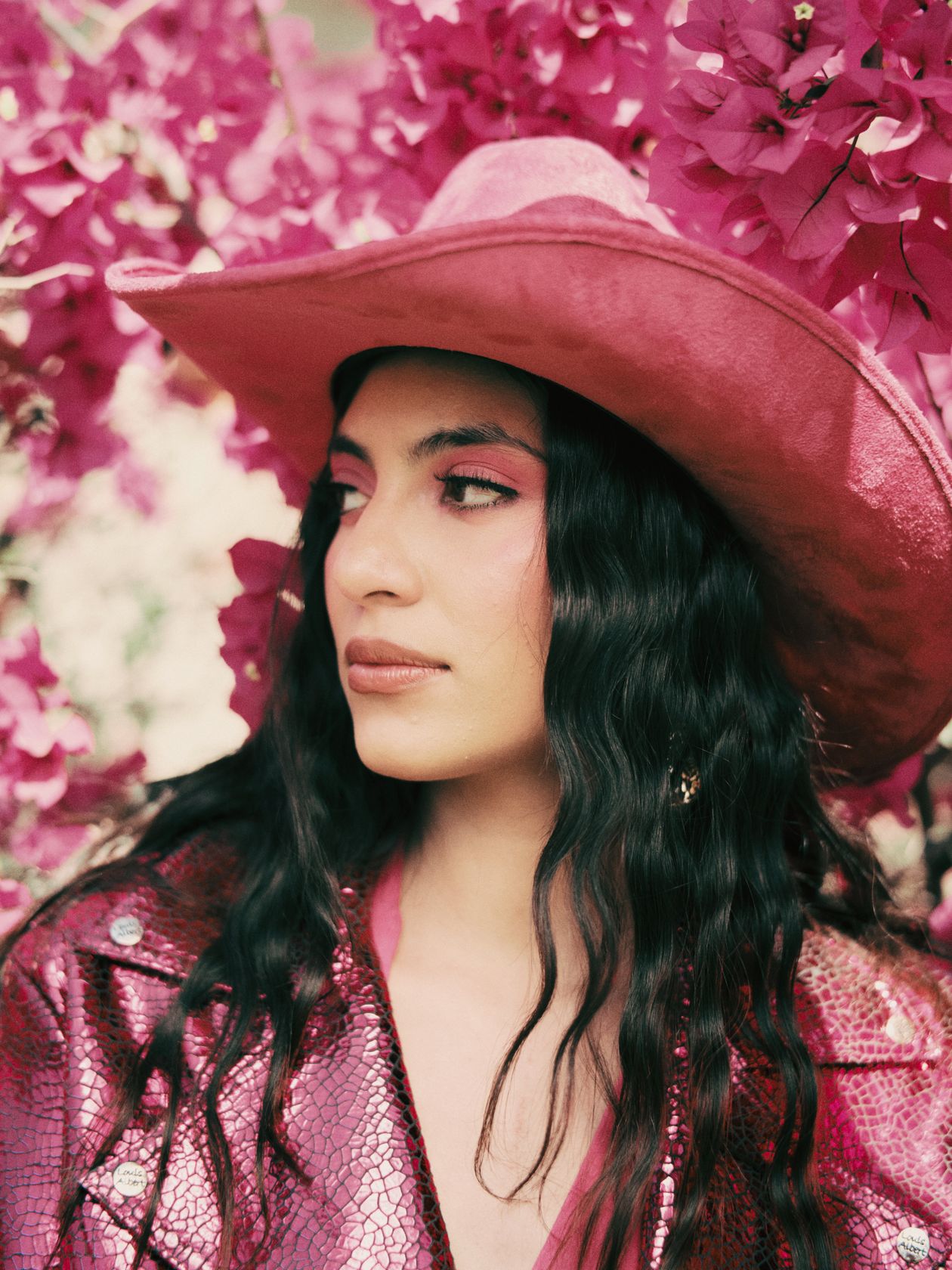 Woman in a pink cowboy hat and shimmery pink jacket among pink flowers