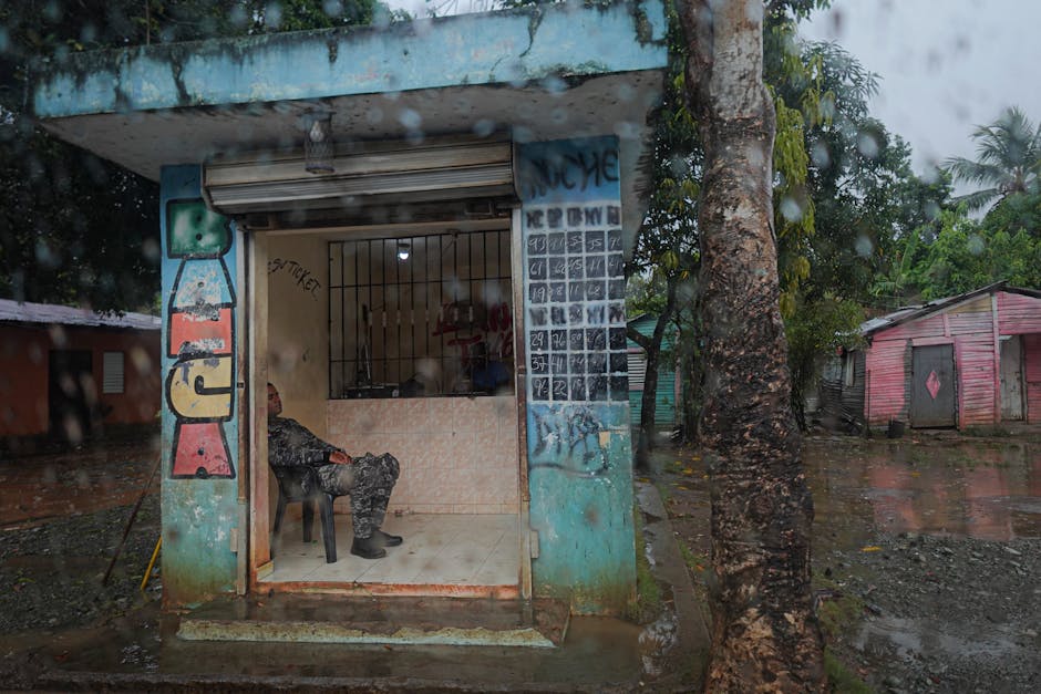 A soldier rests in a small guard post during a rainy day in an urban area.