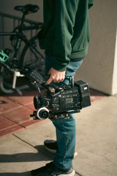 Person holding a professional video camera standing outdoors on a sunny day.