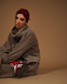 Woman in grey sweater and headband sitting on brown background.