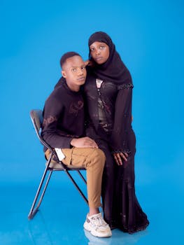 Studio portrait of a diverse couple in traditional and casual attire against a blue background.