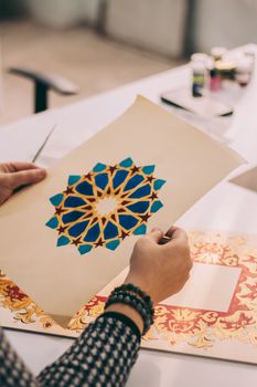 Person working on intricate blue and gold geometric pattern artwork.