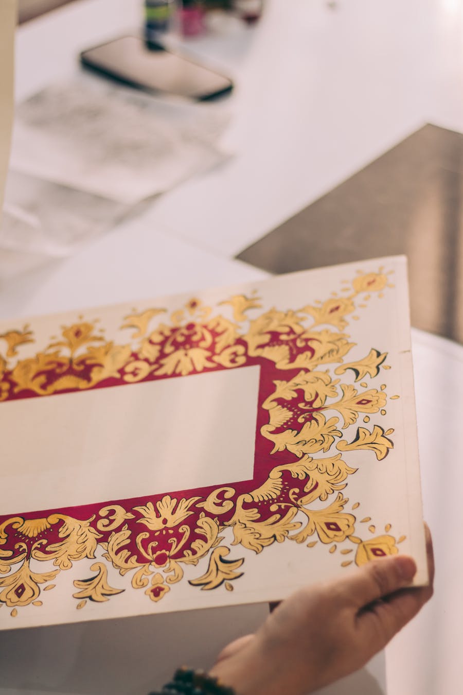 Hand holding an elegant ornate invitation card with intricate golden patterns.