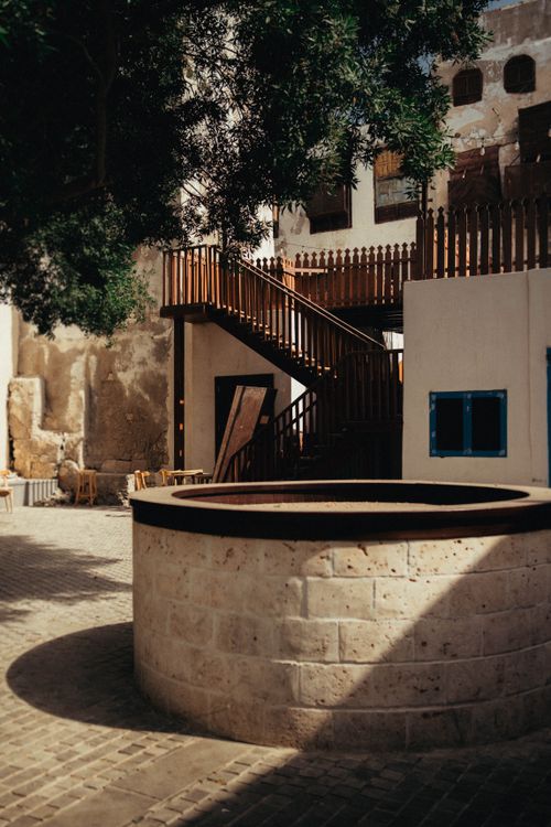 Free Sunlit courtyard featuring a traditional stone well and wooden architecture, showcasing Middle Eastern charm. Stock Photo