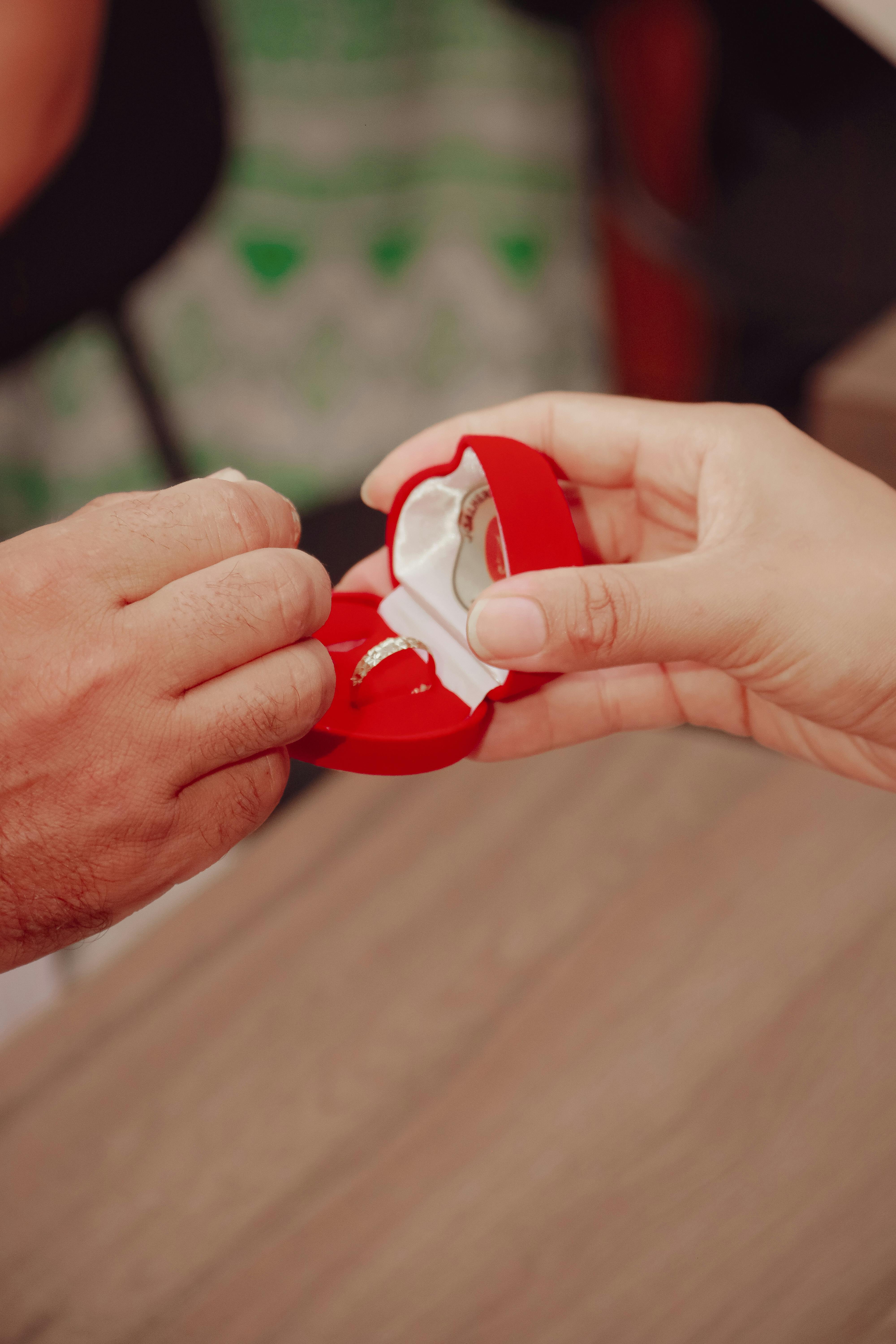 Heartfelt proposal captured with hands exchanging a ring in a red box.