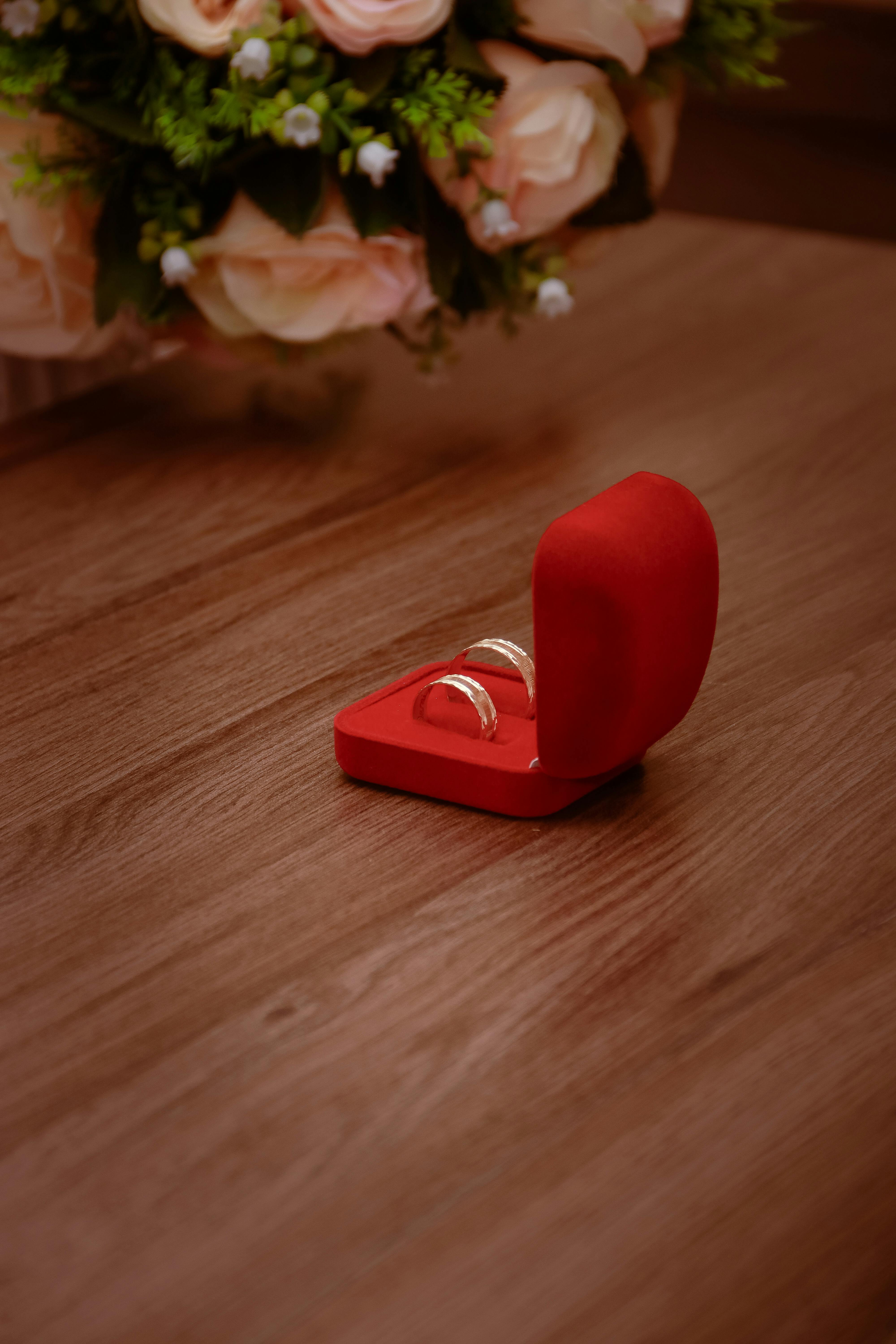 Red velvet ring box with elegant rings on a wooden surface, perfect for weddings or engagements.