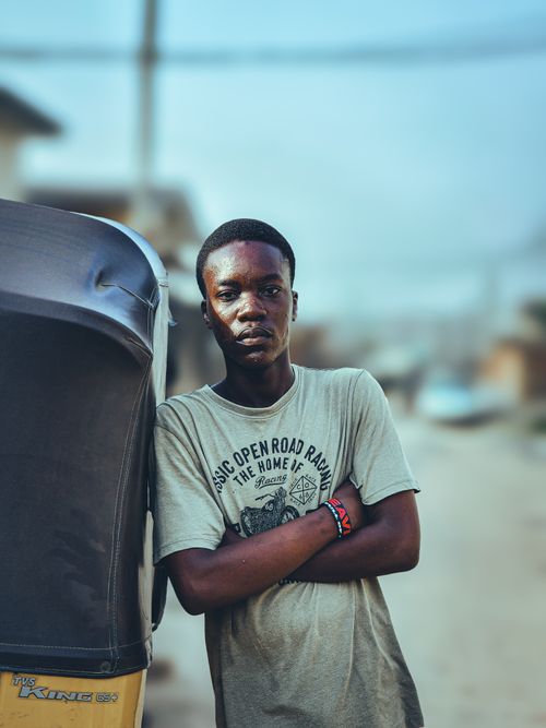 Free A young man stands confidently next to a rickshaw on a sunny day in an urban street. Stock Photo