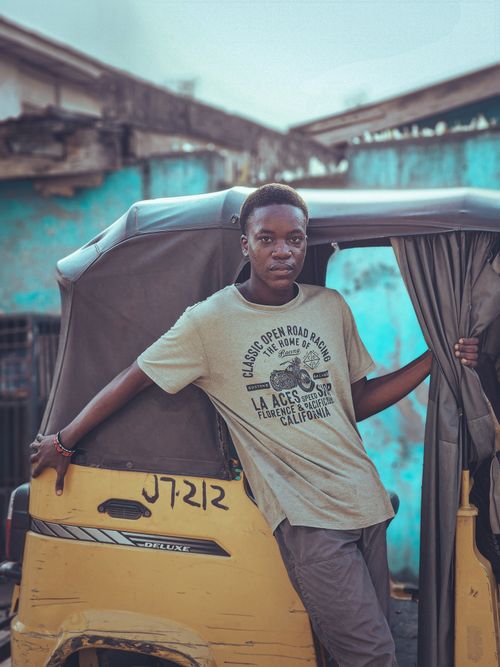 Free Casual young man leaning on a yellow auto rickshaw in an urban setting. Stock Photo