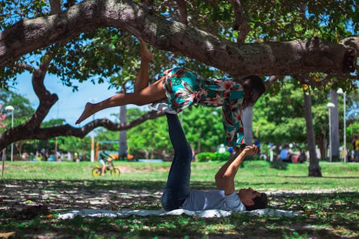 A couple enjoying acro yoga under a tree in a sunny park. Fitness and balance in nature.