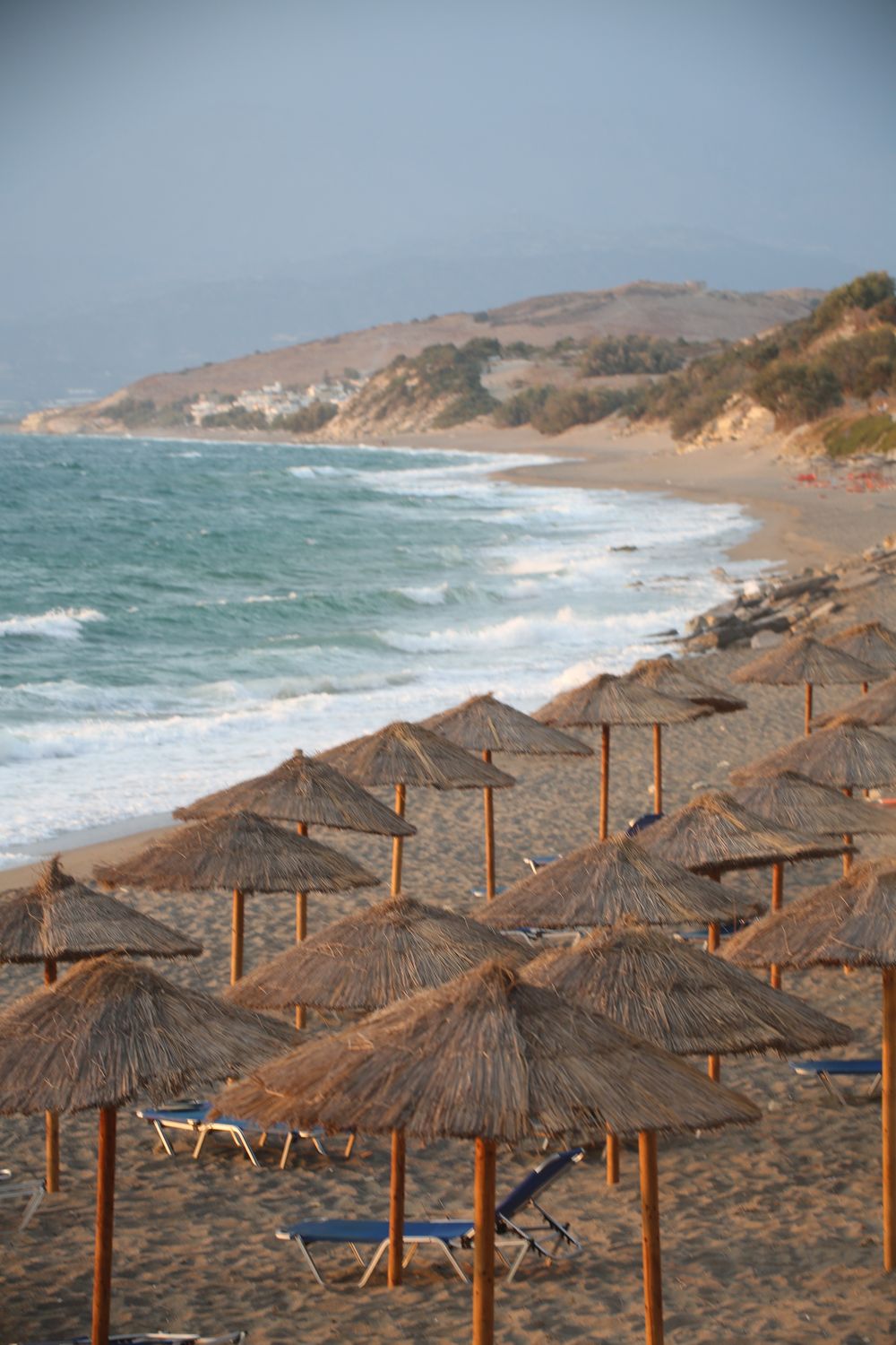 Plajă mediteraneană cu umbrele de paie și apă turcoaz calmă în Grecia