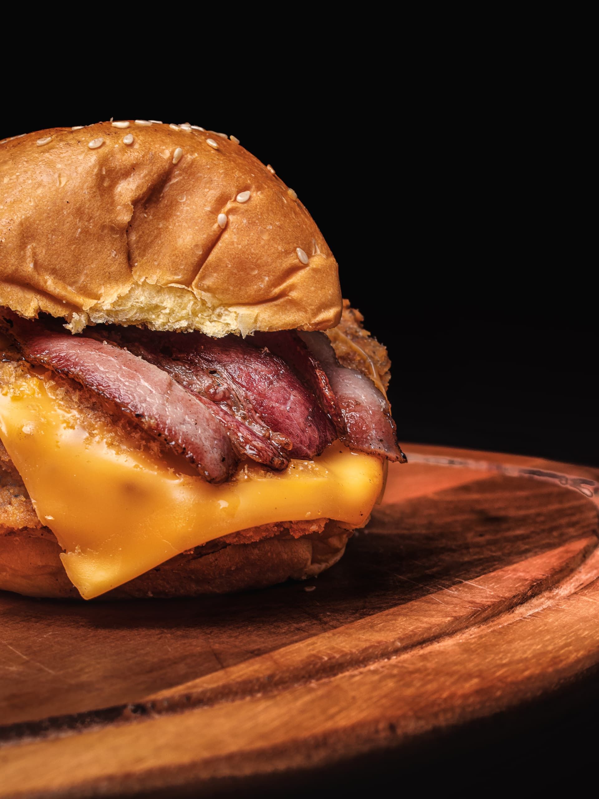 Close-up of a juicy cheeseburger with bacon on a wooden plate, perfect for food lovers.