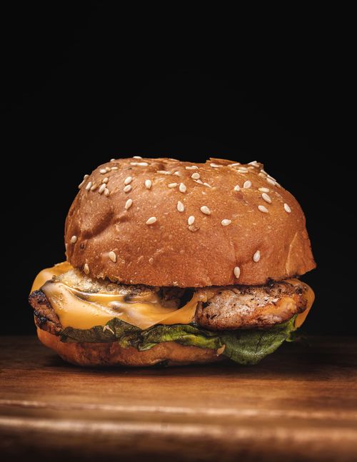 Free Delicious cheeseburger with lettuce, cheese, and sesame seed bun on wooden surface. Stock Photo