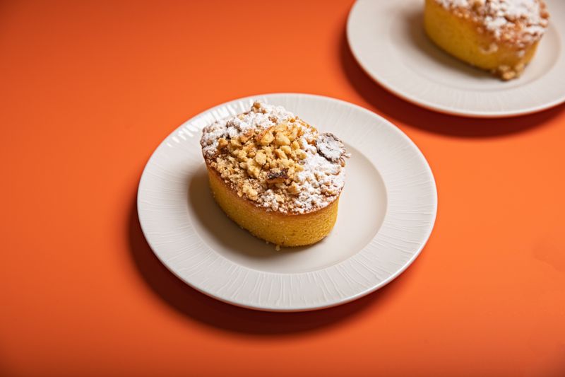 Simple and appetizing crumble-topped muffin on a white plate against an orange background.