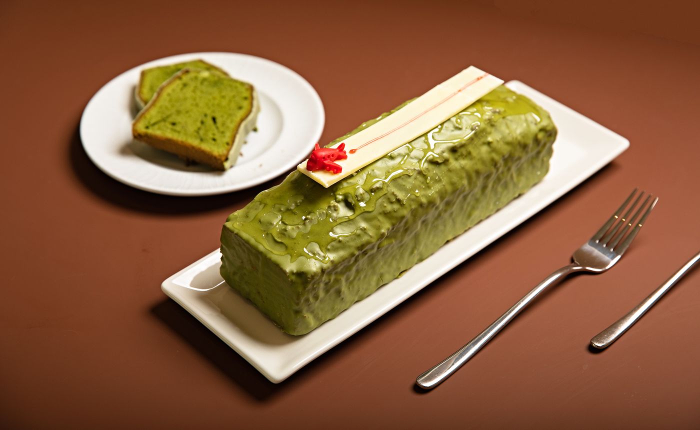 Glazed matcha loaf cake on a white platter with two slices on a separate plate