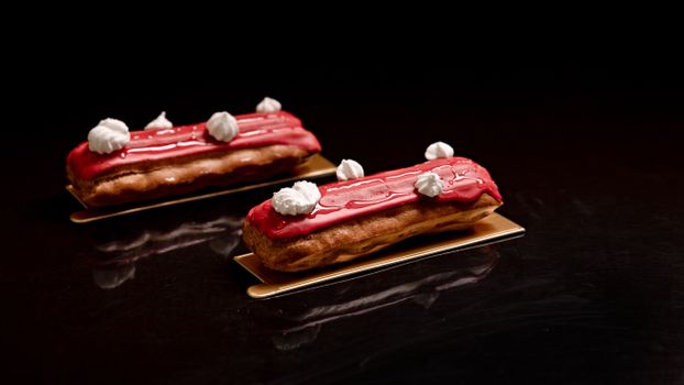 Exquisite red glazed eclairs with white cream decoration, artfully presented on a dark surface.