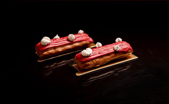 Two eclairs with glossy pink raspberry glaze and small white meringue kisses on gold boards