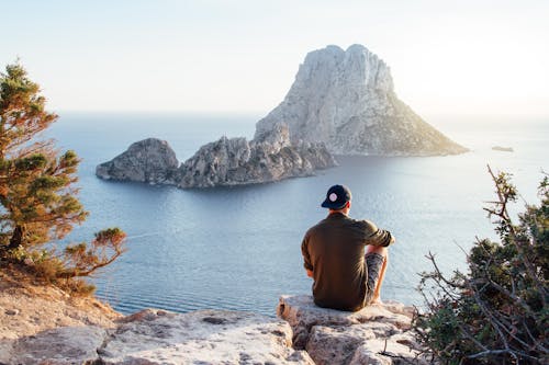 бесплатная Вид сзади человека, сидящего на скале у моря Стоковое фото