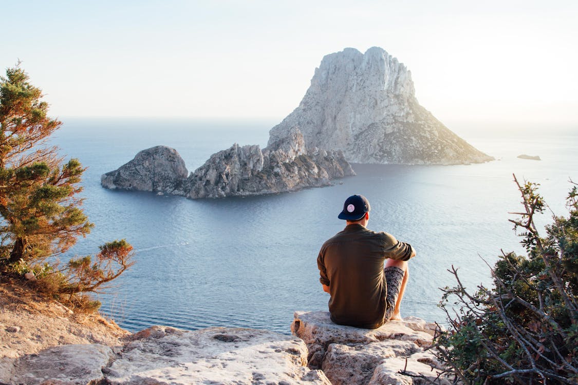 Vista Posteriore Dell'uomo Seduto Su Una Roccia In Mare