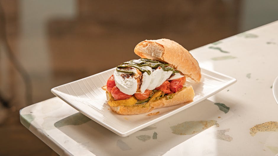 Tasty sandwich with mozzarella, tomatoes, and pesto served on a white plate.