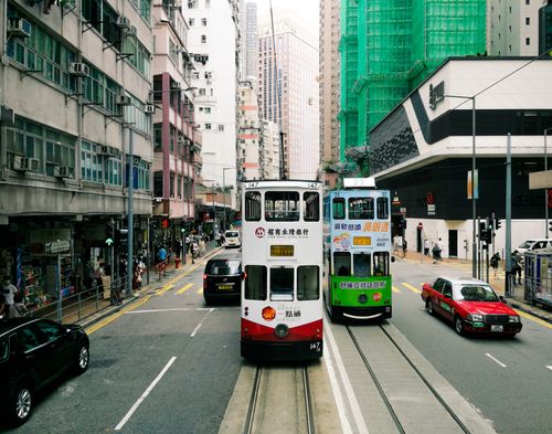 Free Vibrant double-decker trams navigate a busy street on Hong Kong Island. Iconic urban scene. Stock Photo