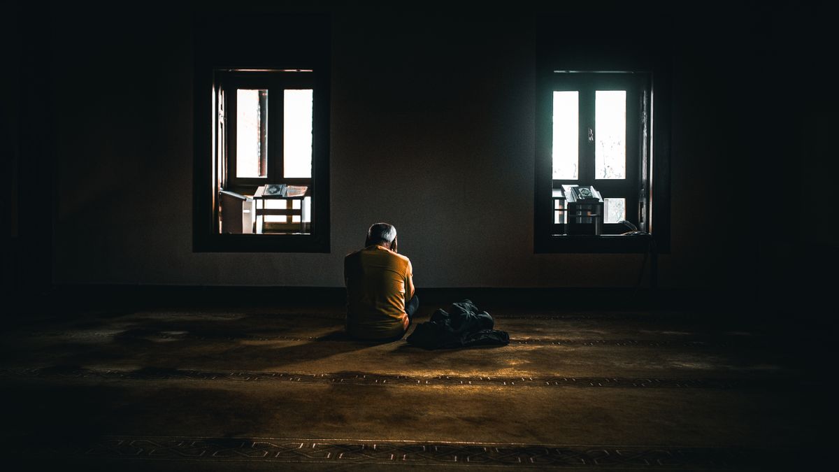 A solitary figure sits in contemplative silence in a dimly lit room with soft natural light.