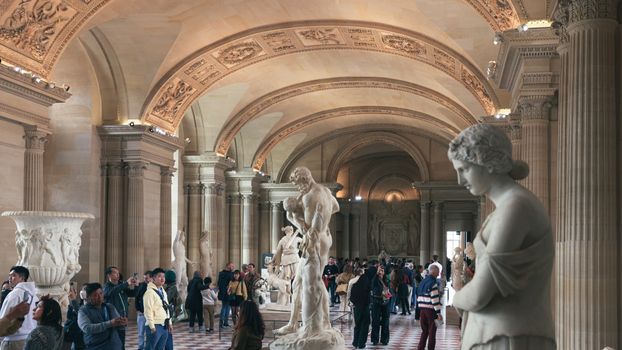 A crowded hall in the Louvre Museum, Paris, showcasing classical statues and architecture.