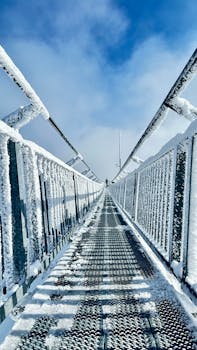 A snow-covered bridge extends towards a clear blue sky, offering a stunning winter scene.