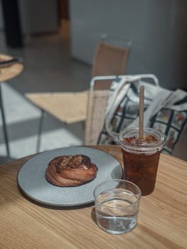 A cozy cafe scene featuring a pastry, iced coffee, and glass of water on a wooden table.