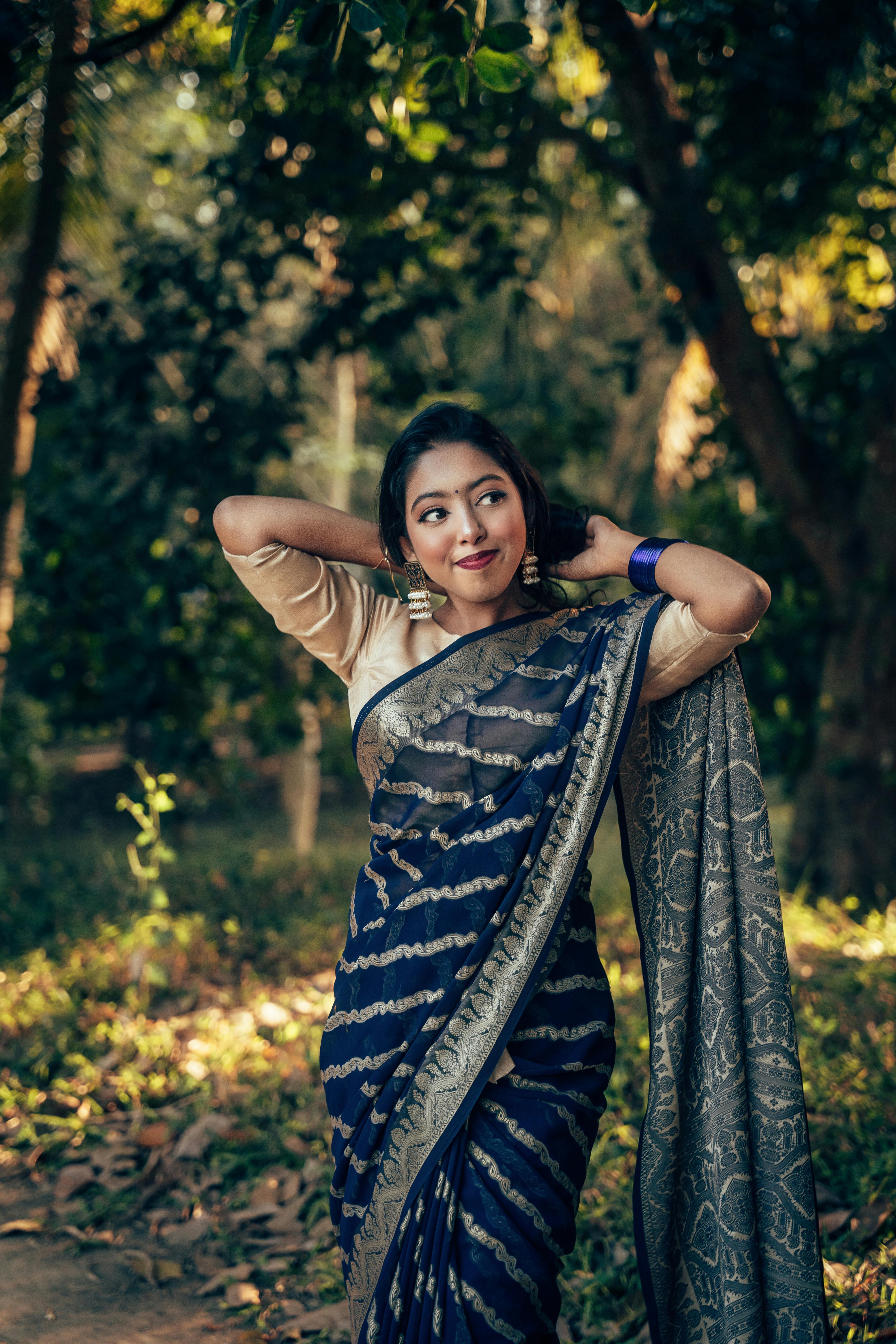 A graceful woman in a traditional saree poses outdoors amidst nature in Comilla, Bangladesh.