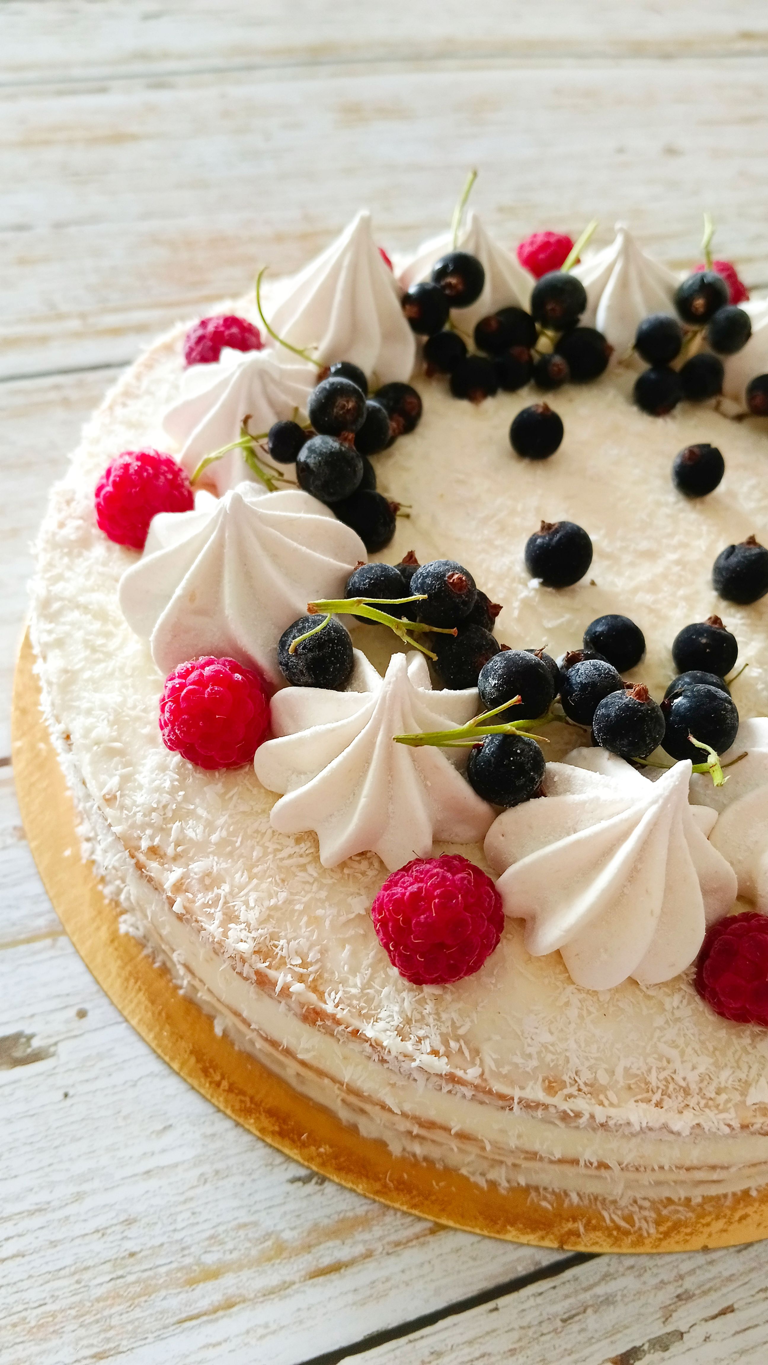 A beautifully decorated homemade cake topped with fresh berries and cream on a rustic wooden table.