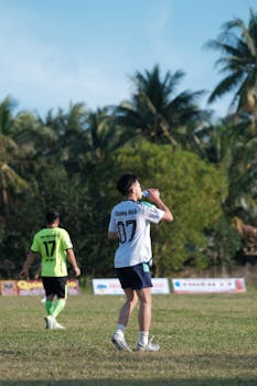 Boys playing a soccer match on a sunny day with palm trees in the background.