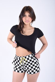 Portrait of a young woman in checkered shorts posing confidently against a white backdrop.
