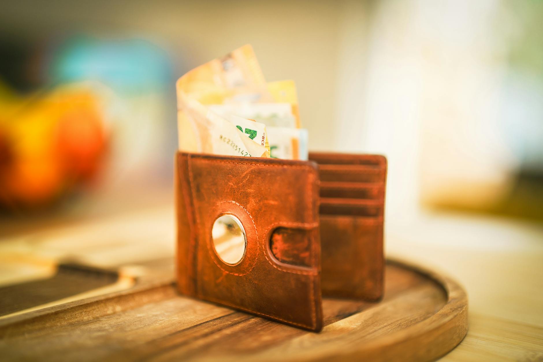 A brown leather wallet filled with various currencies sitting on a wooden table, symbolizing financial savings.