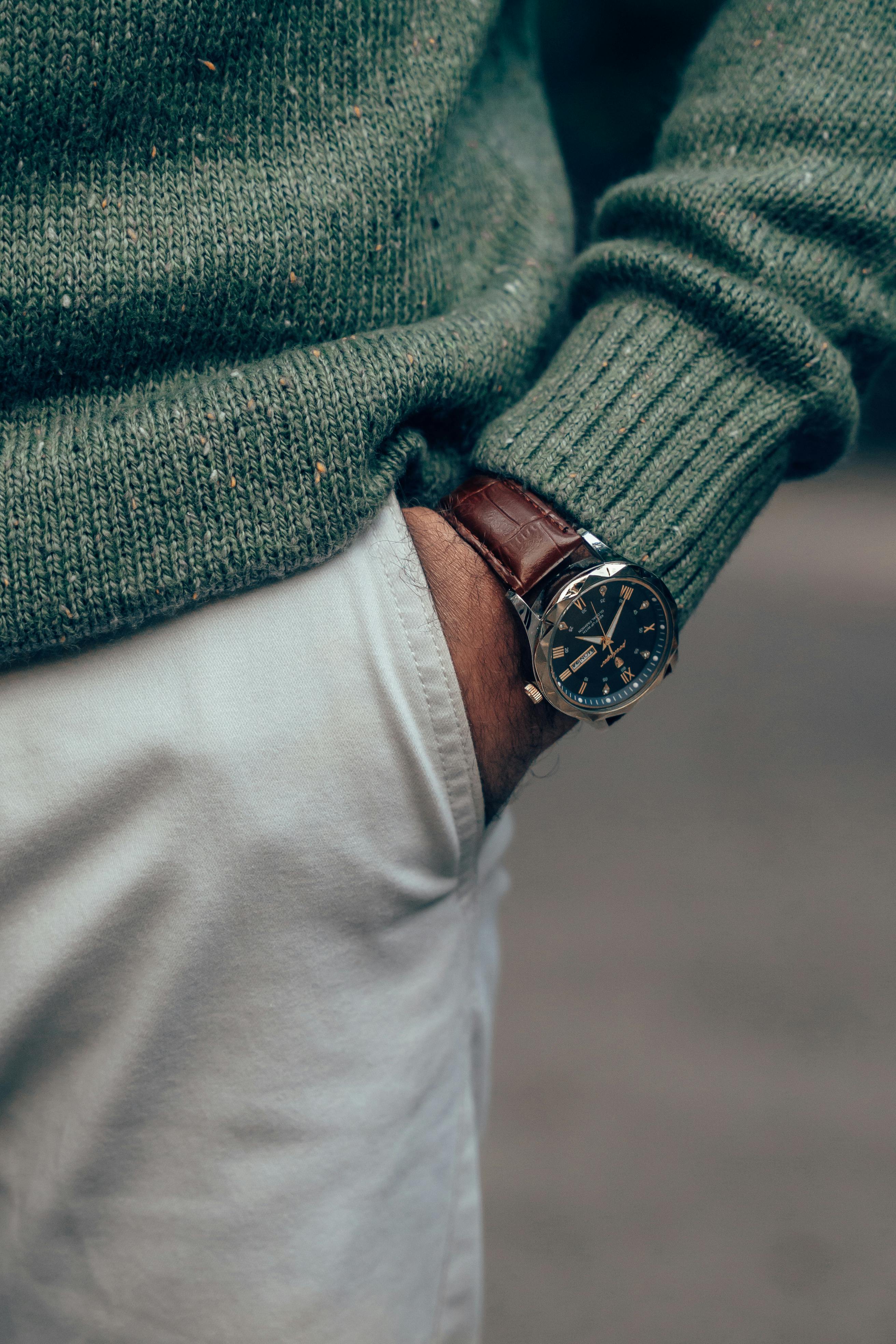Close-up of a stylish wristwatch with a leather band, paired with a green sweater.