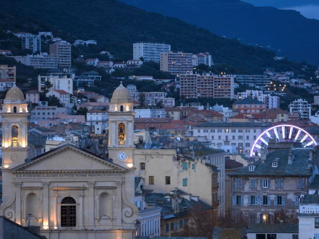 A scenic nighttime view of Bastia, Corse, France featuring a Ferris wheel and illuminated church.