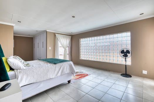 Spacious, minimalist bedroom featuring a large window, neutral tones, and stylish decor.