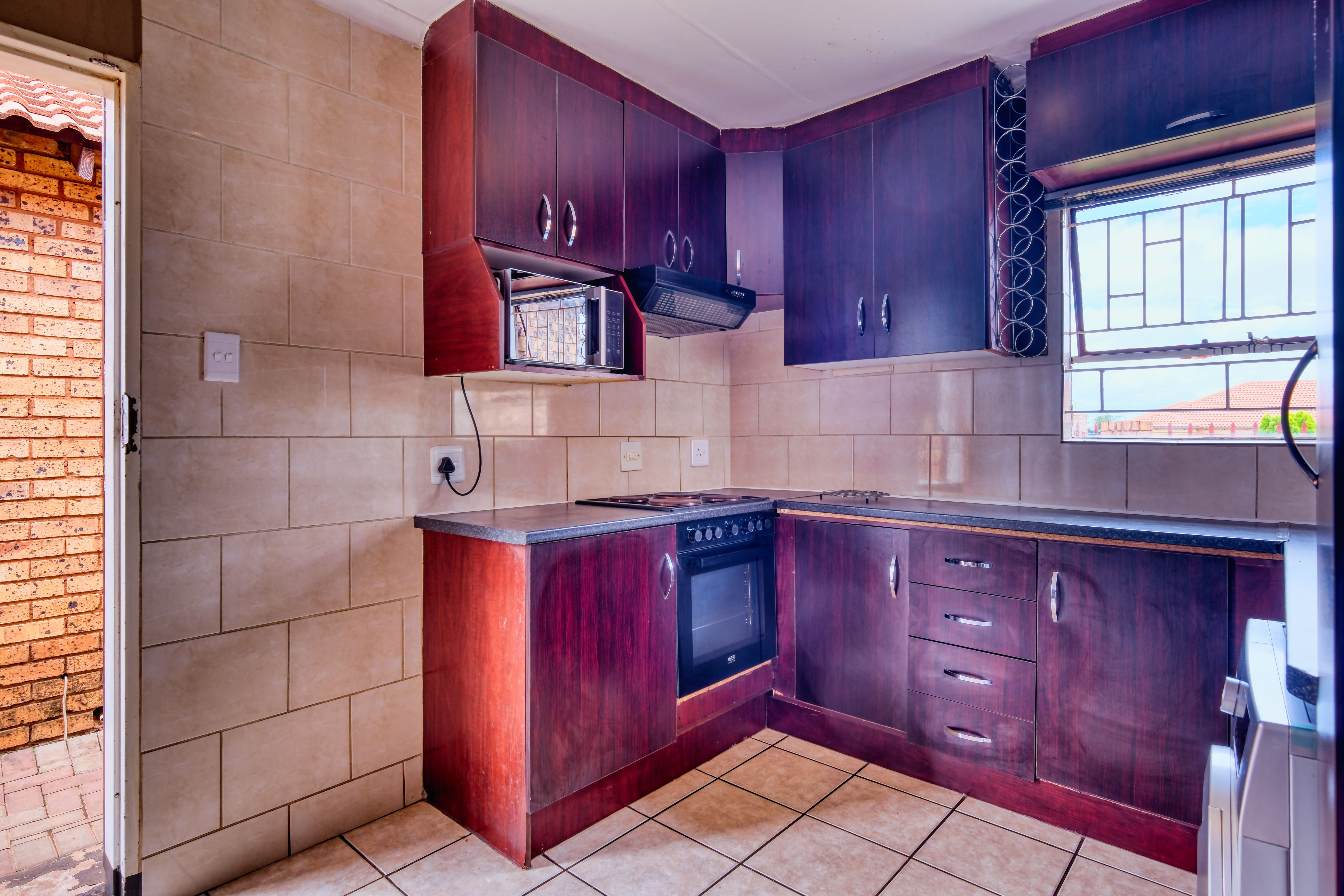 Compact kitchen with dark cabinetry, light wall tile and a pale worktop