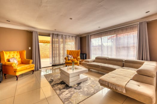 A spacious living room with modern decor featuring bright yellow armchairs and a beige sectional sofa.