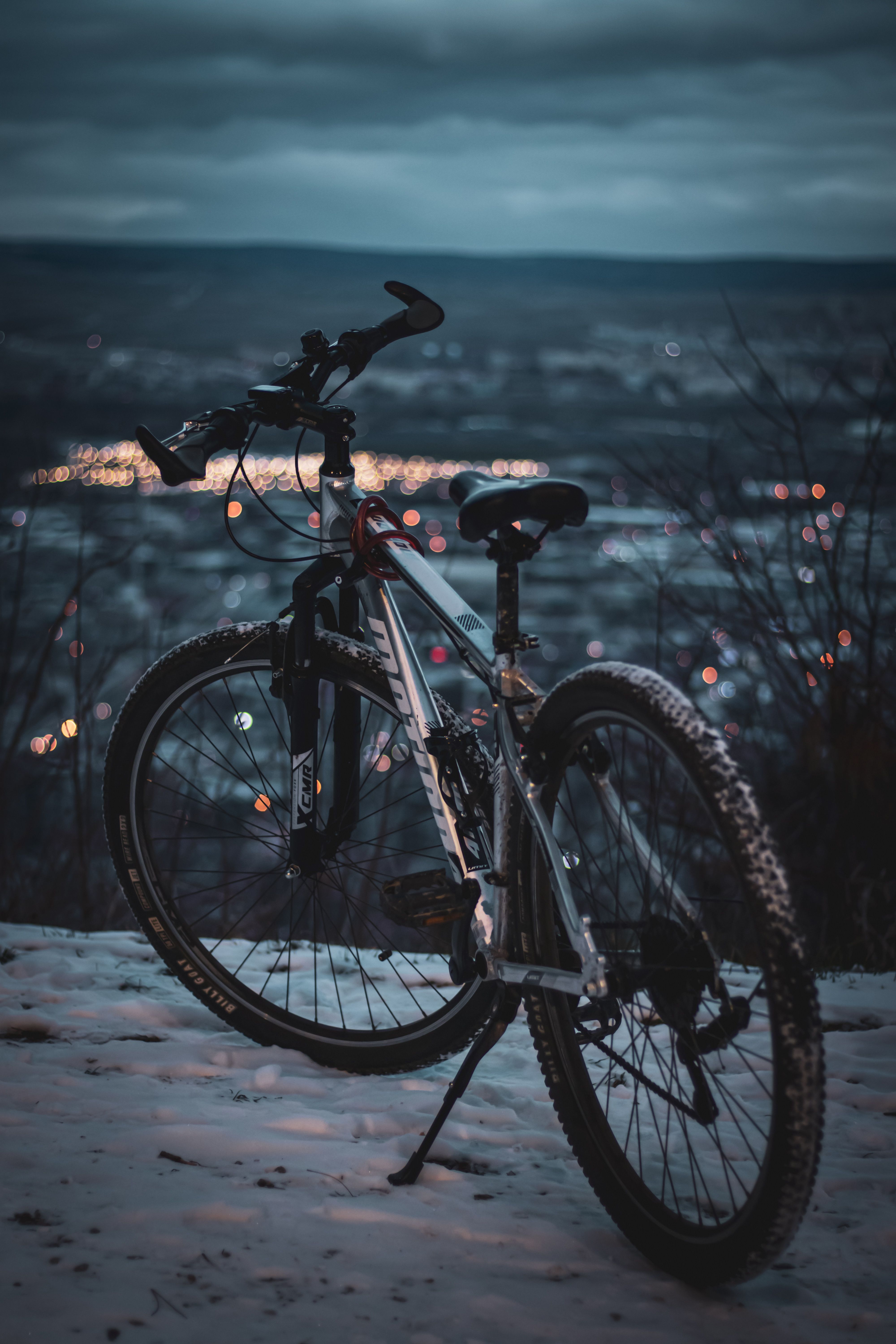 Mountain bike on snowy hill with city lights at dusk, perfect for travel and adventure themes.