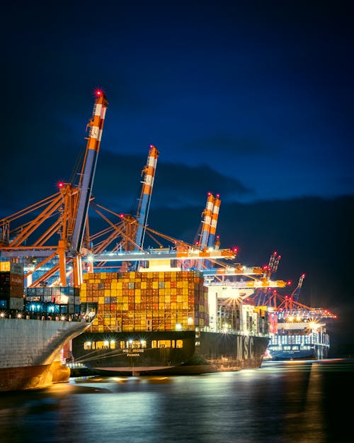 Free Vibrant night view of container ships at Hamburg port with cranes illuminated. Stock Photo