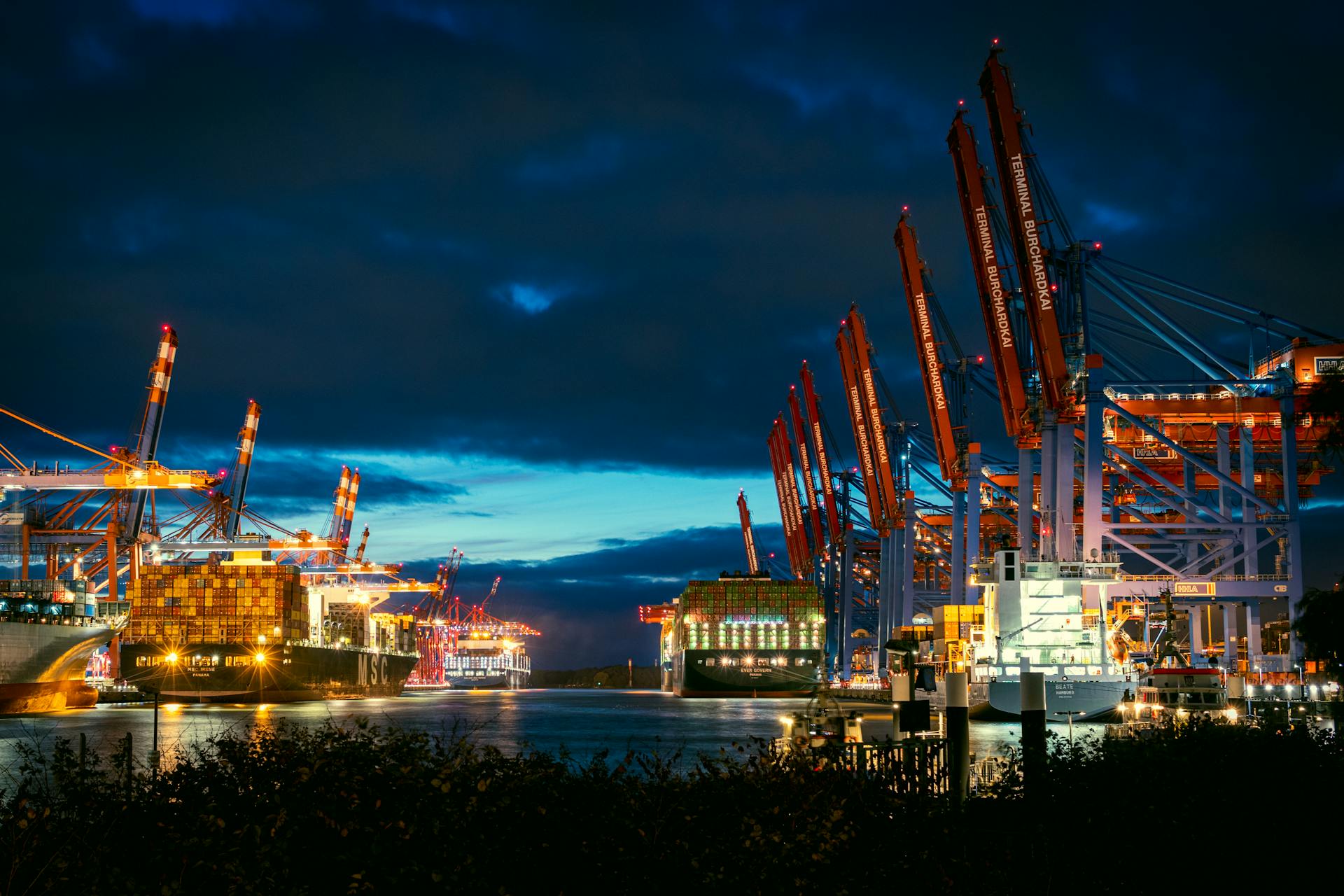 Illuminated cargo port with cranes and ships at night. Maritime industry scene.