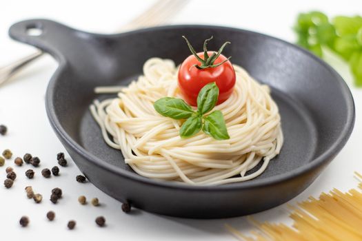 Appetizing spaghetti topped with tomato and basil in a black pan.