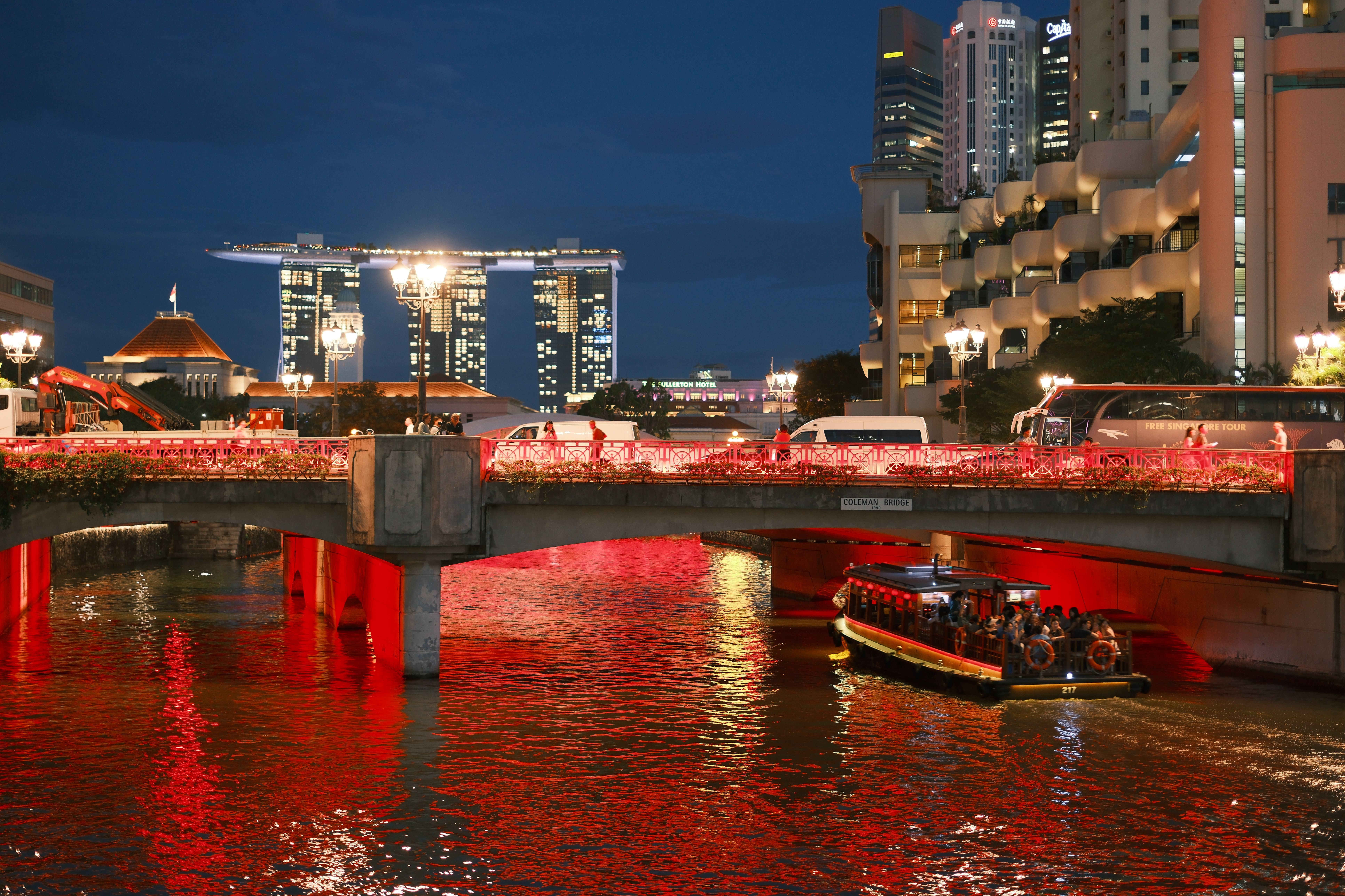 Scenic night view of Marina Bay Sands with vibrant lights and a boat on the river.