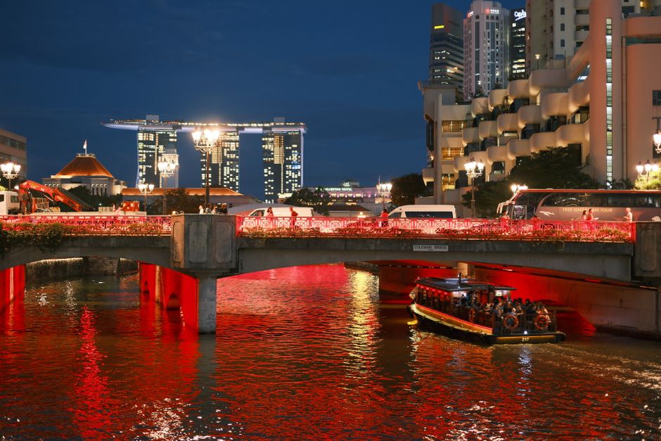 Scenic night view of Marina Bay Sands with vibrant lights and a boat on the river.