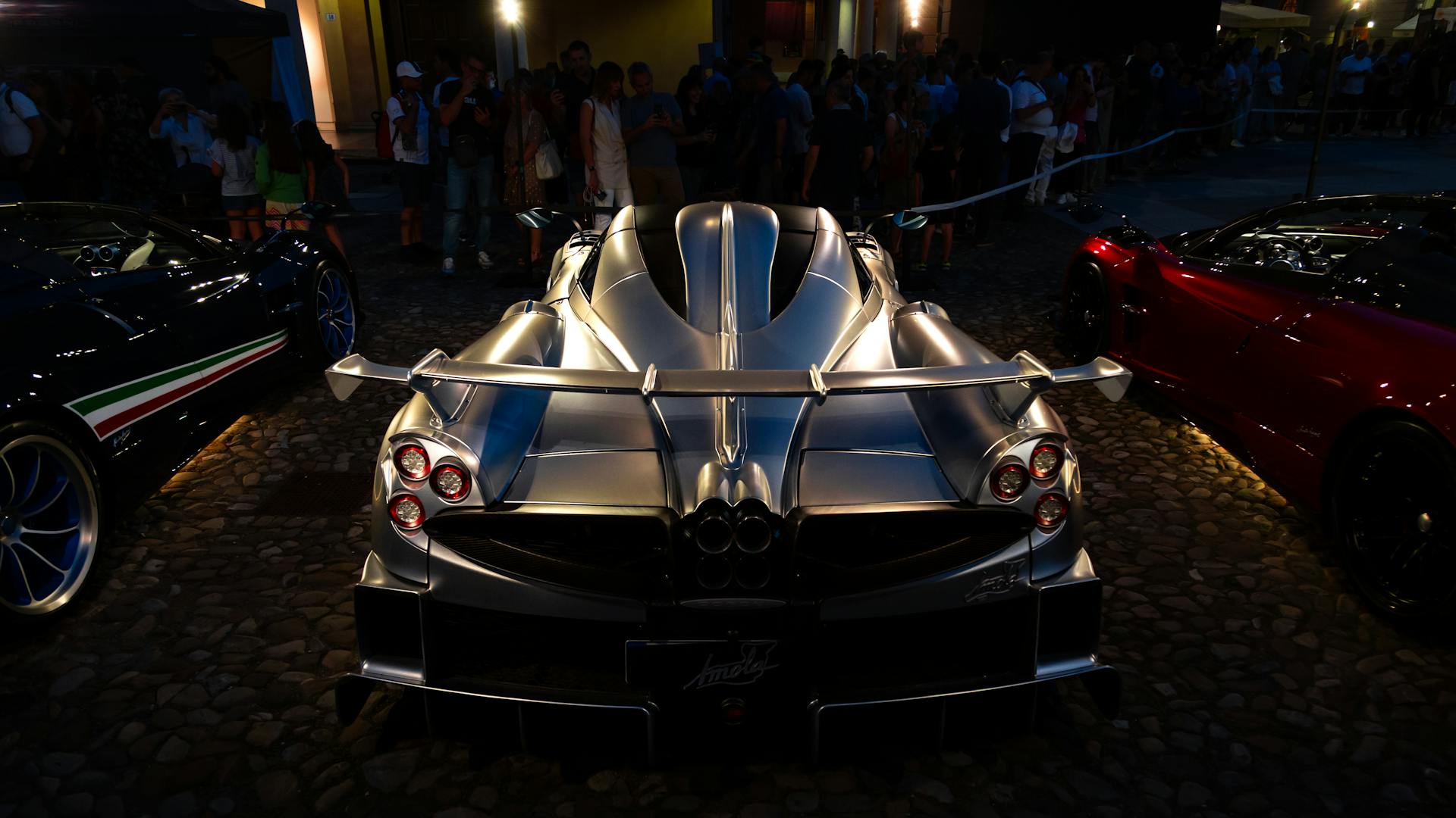 A stunning silver supercar illuminated during a night car exhibition, showcasing its sleek design and luxury features.