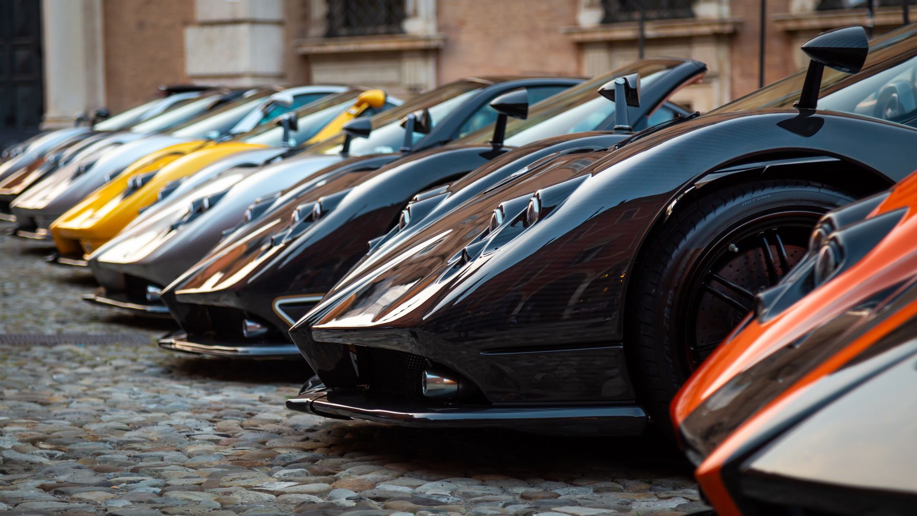 A vibrant lineup of luxury hypercars showcased on a historic cobblestone street in an exhibition setting.
