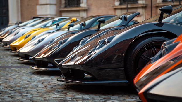 A vibrant lineup of luxury hypercars showcased on a historic cobblestone street in an exhibition setting.