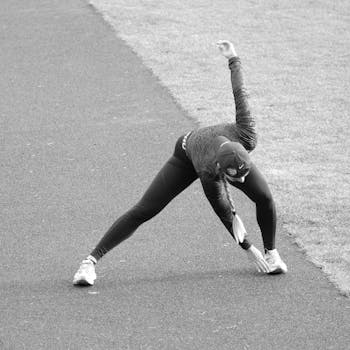 Monochrome image of a person stretching outdoors on a track, emphasizing fitness and flexibility.
