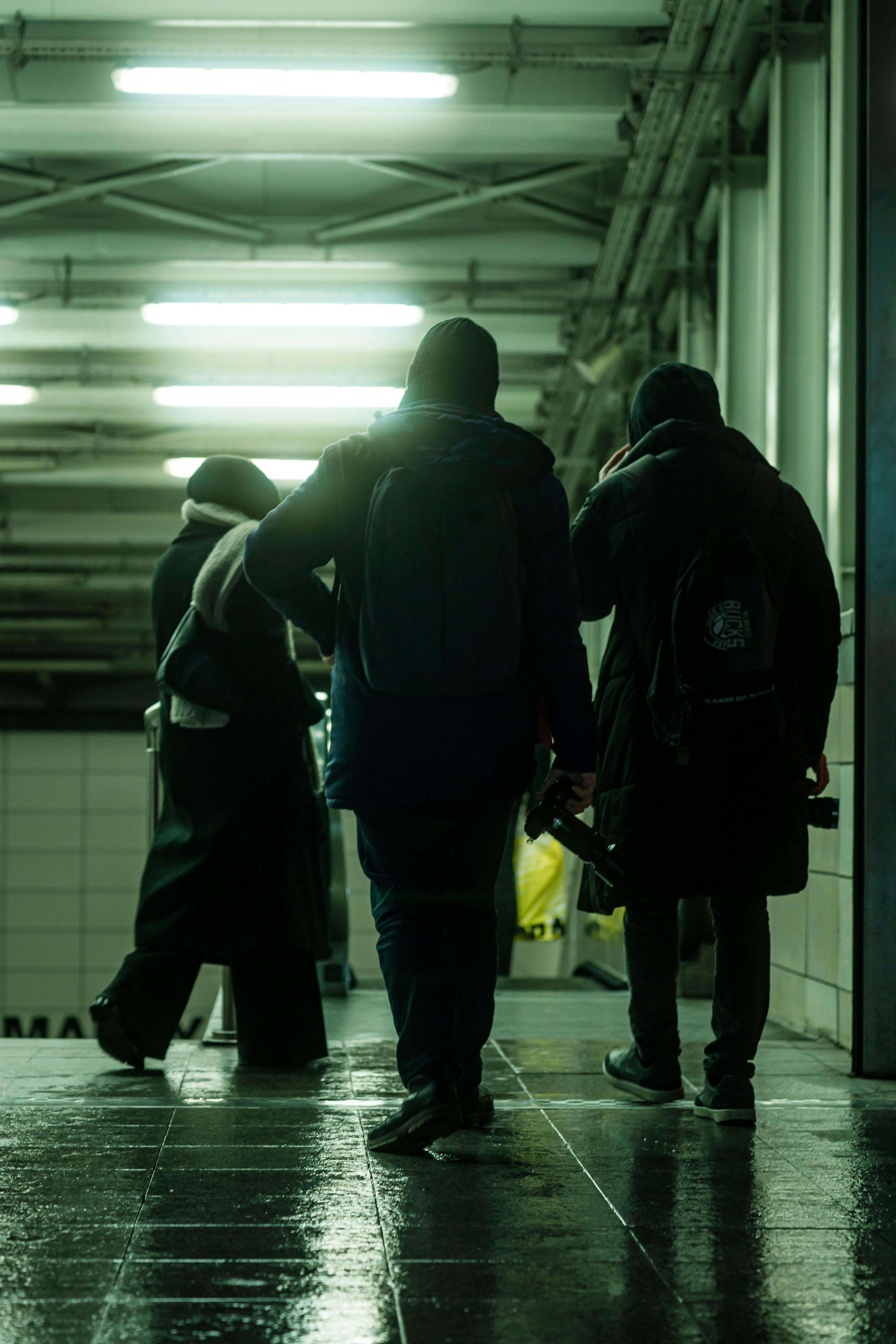 Silhouettes of people walking through a dimly lit subway station at night.