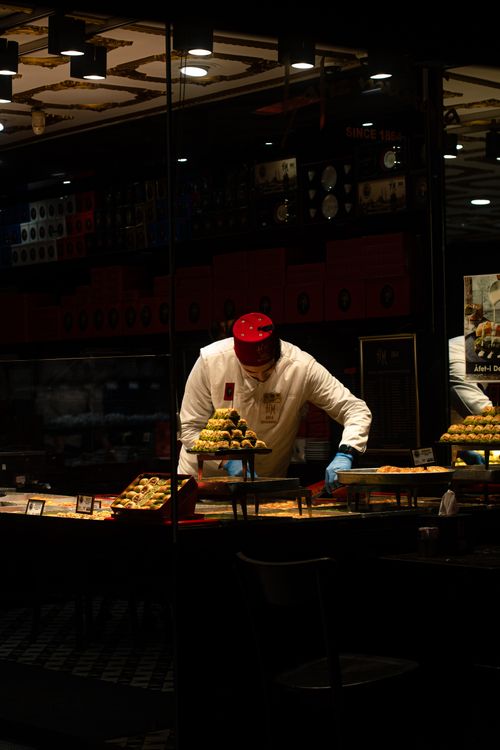 Free Chef organizing pastries at night in a dimly lit bakery. Stock Photo